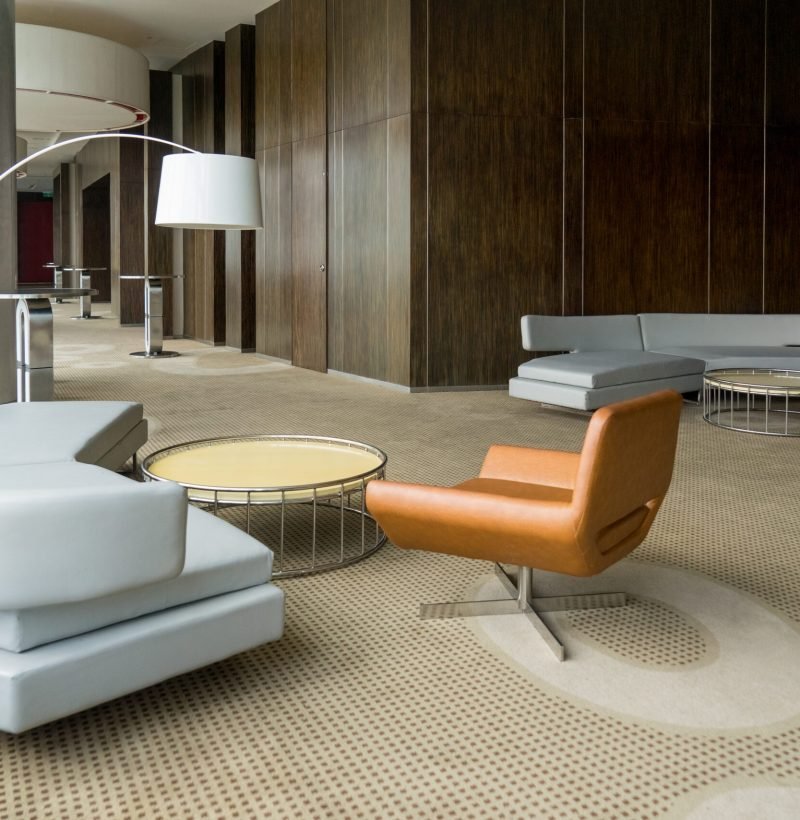 Modern hotel lobby with hallway or office lounge room. Interior with wood paneling, leather sofa and chairs, round metallic tables and floor lamp. Downtown workspace design concept